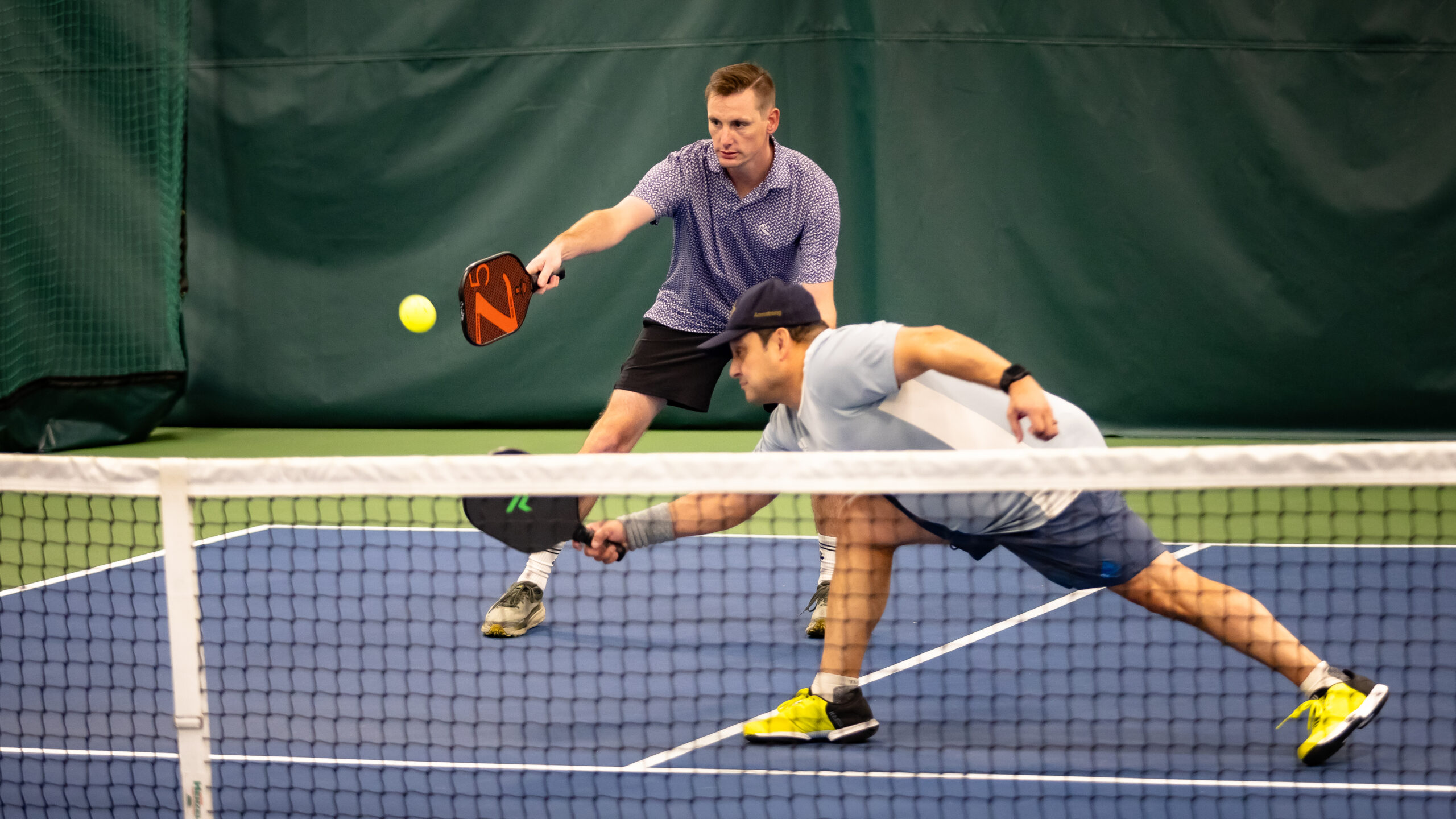 Two players lunging for pickleball at net